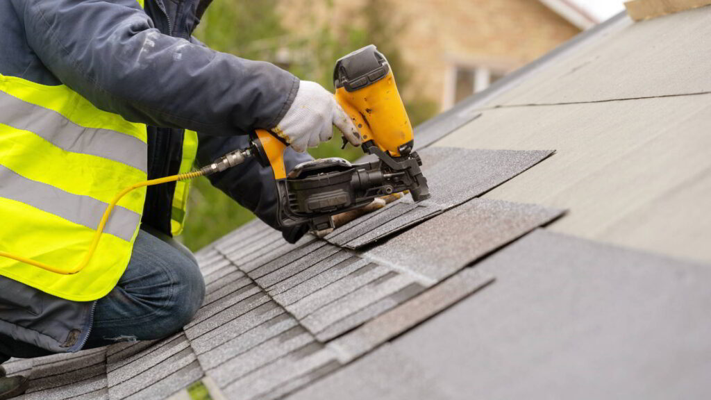 Workman using pneumatic nail gun install tile on roof of new house