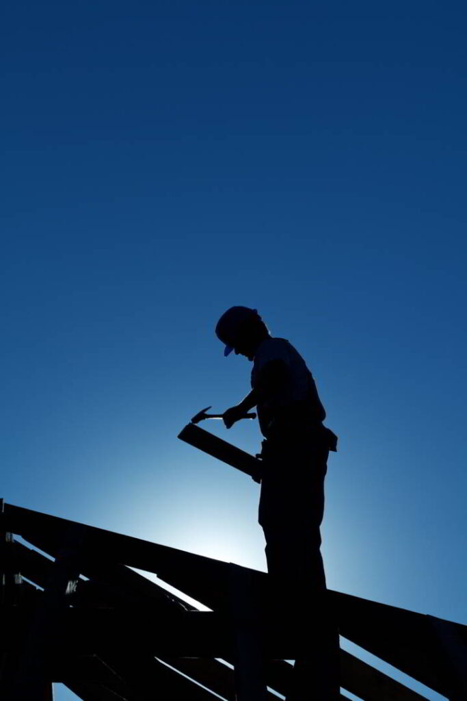 Silhouette of a roofing contractor on top of a roof.