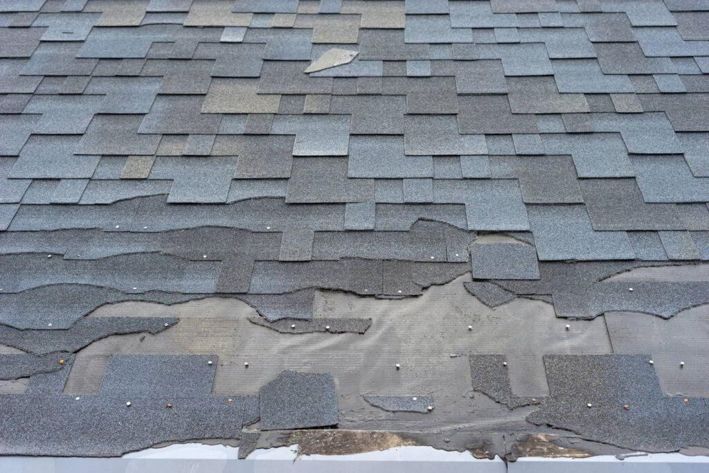 Сlose up view of bitumen shingles roof damage that needs repair.